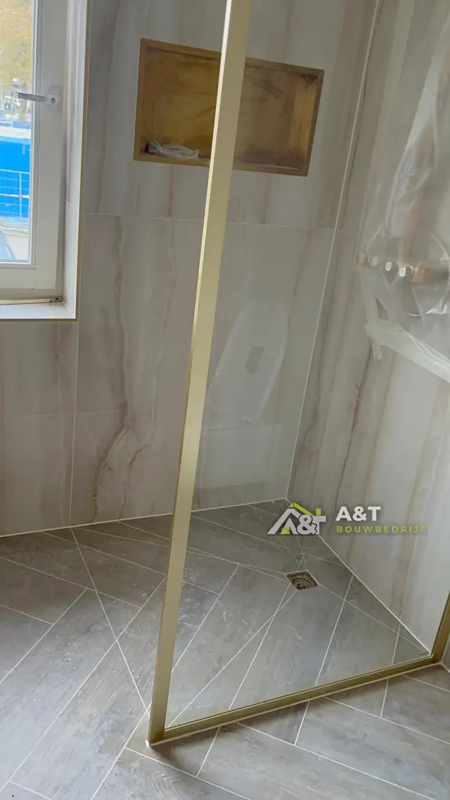 Douche met gouden nis. Houtlook-wandtegels, visgraatvloer en een goudkleurige nis en douchewand.