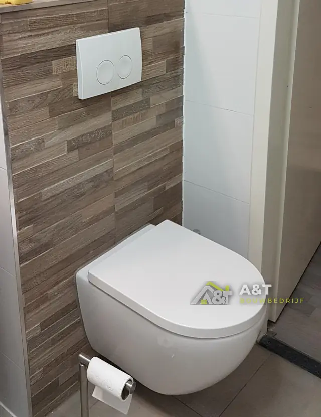 Toilet met ombouw in houtlook. Voorzetwand betegeld in houtlook, hangtoilet en witte bedieningsplaat.