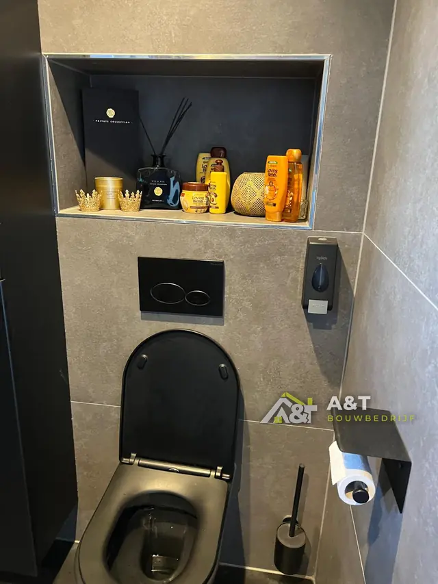 Zwart hangtoilet met nis. Grote grijze tegels, een ingebouwde nis en zwarte bedieningsplaat.